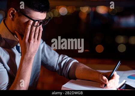 Businessman Touching Eye Under Glasses Working In Office At Night Stock Photo