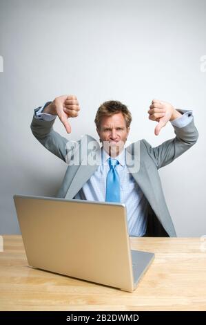 Office worker at his computer looking at the camera with a frown and two thumbs down Stock Photo