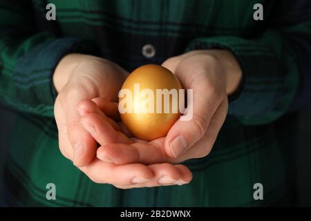 Woman in shirt holds golden egg, close up Stock Photo