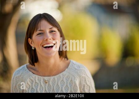 Portrait of a smiling young woman relaxing in a sunny park Stock Photo