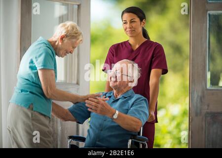 Senior man being pushed in a wheelchair by a young nurse is delighted to meet an old friend Stock Photo