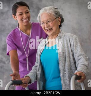 Smiling elderly woman using her walker assisted by a friendly young nurse Stock Photo
