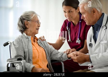 Doctor and nurse talking to a senior patient sitting in a wheelchair Stock Photo