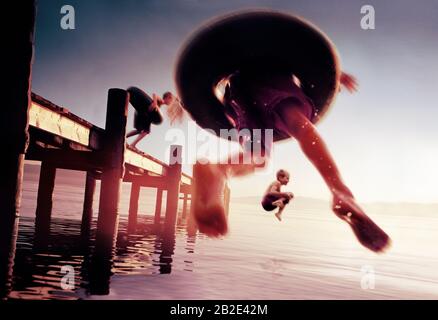 Three young boys having fun jumping of the edge of a pier and into the sea. Stock Photo