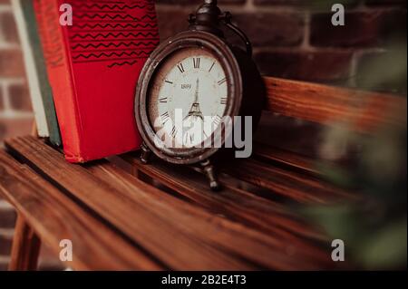 old antique broken clock without arrows with the image of the eiffel tower in a wooden bookcase on the background of books Stock Photo