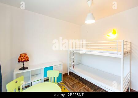 Children's room in the cottage. Bunk bed, window with blue curtains, large wardrobe with yellow doors. Stock Photo