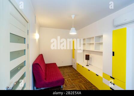 Children's room in the cottage. Bunk bed, window with blue curtains, large wardrobe with yellow doors. Stock Photo