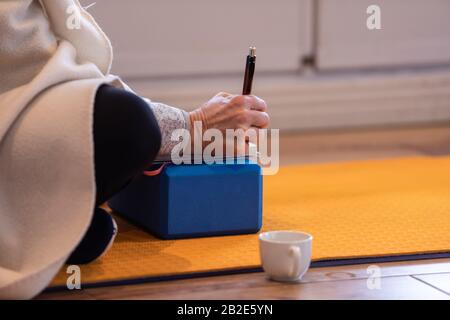 A person making notes in his or her notepad during the yoga class in some kind of pose of yoga. An apprentice learning more about yoga Stock Photo