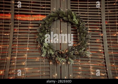 beautiful Christmas tree wreath hanging on a wall of wood and brick with many light bulbs and garlands hanging down Stock Photo