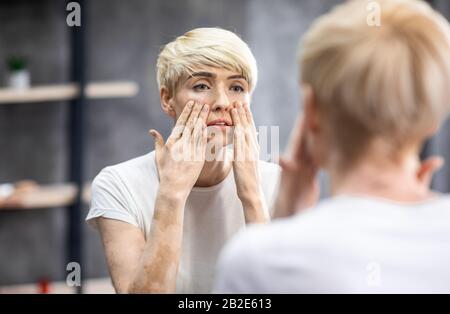 White Caucasian dyed blonde middle aged woman in her 40s wearing a blue shiny  PVC raincoat purchased from a second hand shop. Sat on rocks looking  thoughtful Stock Photo - Alamy