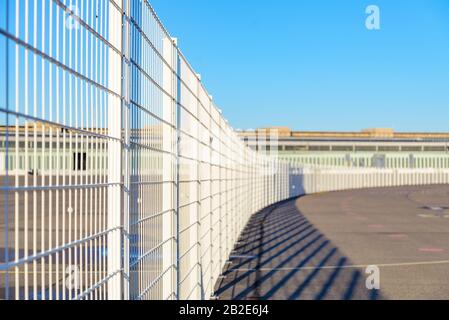 Diminishing perspective view of tall white grid metal curved fence on old landing field in former military airport in Berlin, Germany. Stock Photo