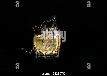 aqua water with lemon soda spills when ice is thrown with drops on a black background Stock Photo