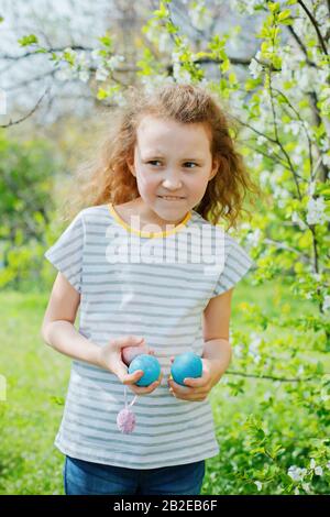 Easter egg hunt concept. Little girl keeps colorful painted eggs on Easter Day. child hunting eggs in grass. Vertical Stock Photo