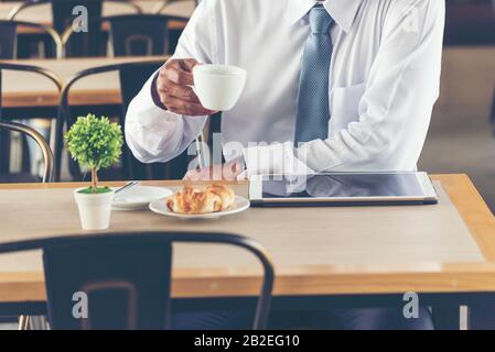 Asian Handsome businessman working outdoor in the coffee shop with laptop and holding cup of coffee on hand. Work outside office using technology with Stock Photo