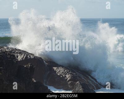 Waves, Explosion of water a wave smashing into and crashing against and  onto rocks by the sea, Sawtell Australia Stock Photo