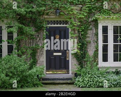 vine covered entrance of old brick house with lion head knocker on front door Stock Photo