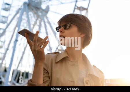 Teen girl using phone voice recognition record audio message on city street. Stock Photo