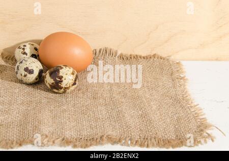 Three quail eggs and one chicken egg on a rough canvas. Stock Photo