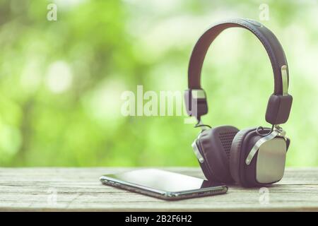 Close up new smartphone and headphone on wooden table with green space nature blur background Stock Photo