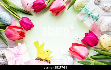 Spring tulip flowers, Easter eggs, gift box and paper card on old white table from above in flat lay style. Greeting for Easter.  Top view, flat lay. Stock Photo