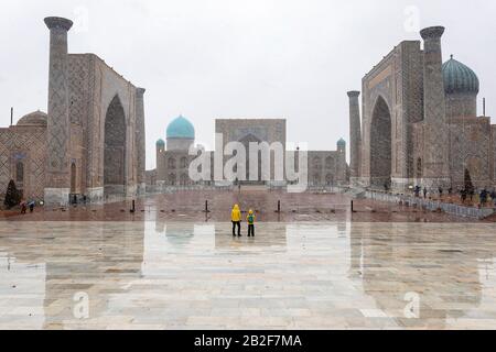 Mother and son in yellow rain jackets in the Registan, the heart of the ancient city of Samarkand - Uzbekistan, falling snow Stock Photo