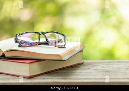 Close up book and eye glasses on wooden table with abstract green nature blur background. Reading and education concept Stock Photo