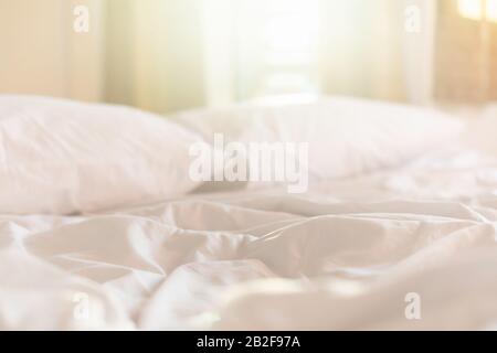 Close up white bedding sheets and pillow in hotel room at morning time with sunlight from windows Stock Photo