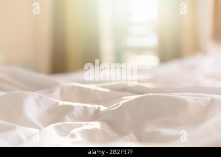 Close up white bedding sheets and pillow in hotel room at morning time with sunlight from windows Stock Photo