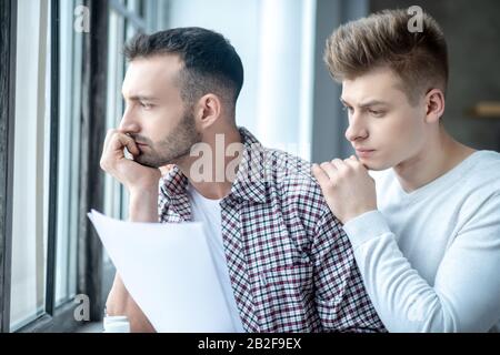 Two young men standing near the window looking desperate Stock Photo