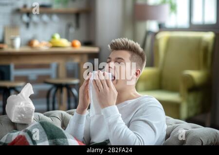 Fair-haired young man holding a napkin and sneezing Stock Photo