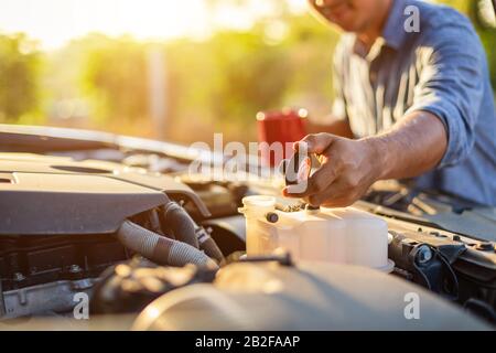 Asian man holding a red coffee cup and checking the engine of his car in the morning. Car maintenance or service before driving concept Stock Photo