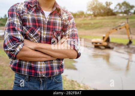 Asian young engineer working on site at the dam and control while excavator digging the earth Stock Photo