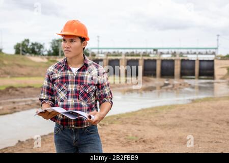 Asian young engineer working on site at the dam and control while excavator digging the earth Stock Photo