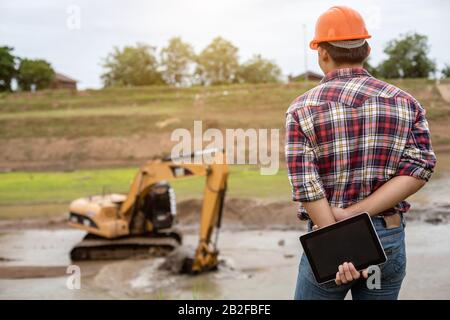 Asian young engineer working on site at the dam and control while excavator digging the earth Stock Photo