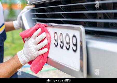 Man using red cloth to cleaning front car plate number. Cleaning car concept Stock Photo