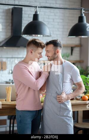 Two young men standing hugging in the kitchen. Stock Photo