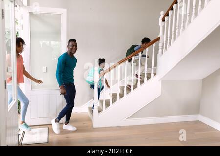 Side view of an African American couple with young son and daughter entering the front door and walking up the stairs in their new home. Family enjoyi Stock Photo