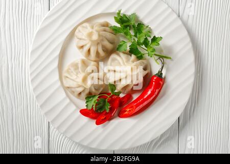a portion of Khinkali, dumplings with meat filling served on a white plate with parsley and chili, georgian cuisine, horizontal view from above, close Stock Photo