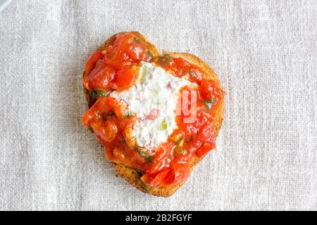 Bruschetta with ricotta cheese and tomato sauce on fabric background in a form of heart Stock Photo