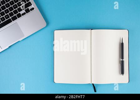 open diary or notebook with blank white pages and laptop computer on blue background template Stock Photo