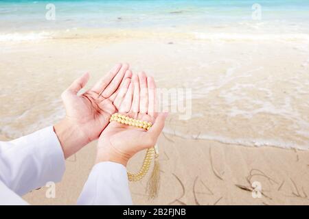 Muslim man praying with prayer beads on his hands on the beach Stock Photo