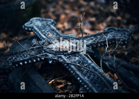 A beautiful old stone cross with a pattern is laid on the grave, and on it lie the curved branches of trees and fallen dry leaves. Autumn is the perso Stock Photo