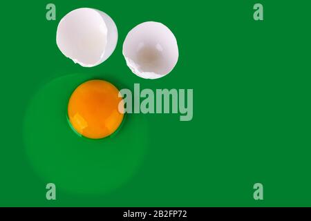 Raw egg, yellow yolk and white shell eggs on green background top view close up, uncooked broken egg backdrop, Easter banner, creative paschal poster Stock Photo