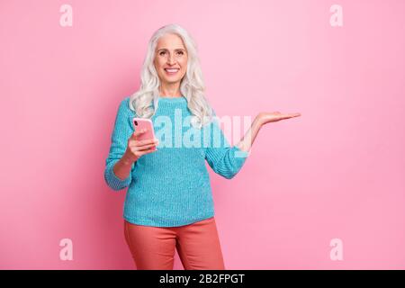 Portrait of positive cheerful old woman promoter use smartphone hold hand recommend online product ads promotion wear casual style sweater isolated Stock Photo