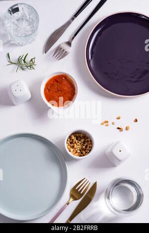 Empty round blue and purple plates with cutlery , roasted peanuts and tomato sauce on white background. Top view with copy space for you design. Stock Photo