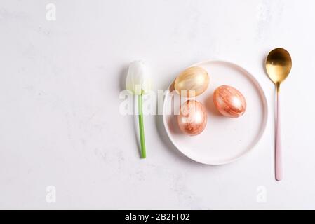 Easter plate with spring tulips and spoon and golden eggs on a stone Stock Photo