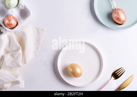 Easter table setting from above. Elegant empty plate, cutlery, napkin and golden eggs on stone Stock Photo