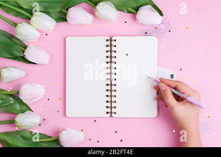 Pastel Tulips with notebook and hand hold a pen on pink background with stars, copy space Stock Photo