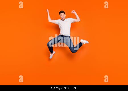 Full size photo of crazy funny energetic delighted guy celebrate lucky lottery win jump raise fists scream yeah wear casual style clothes isolated Stock Photo