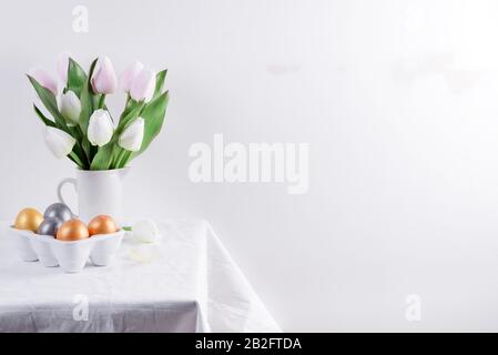 Golden Easter Eggs in ceramic egg tray with tulip on white table. Easter background or easter concept. Stock Photo